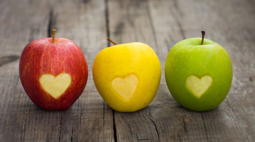 Three different coloured apples with hearts carved on them