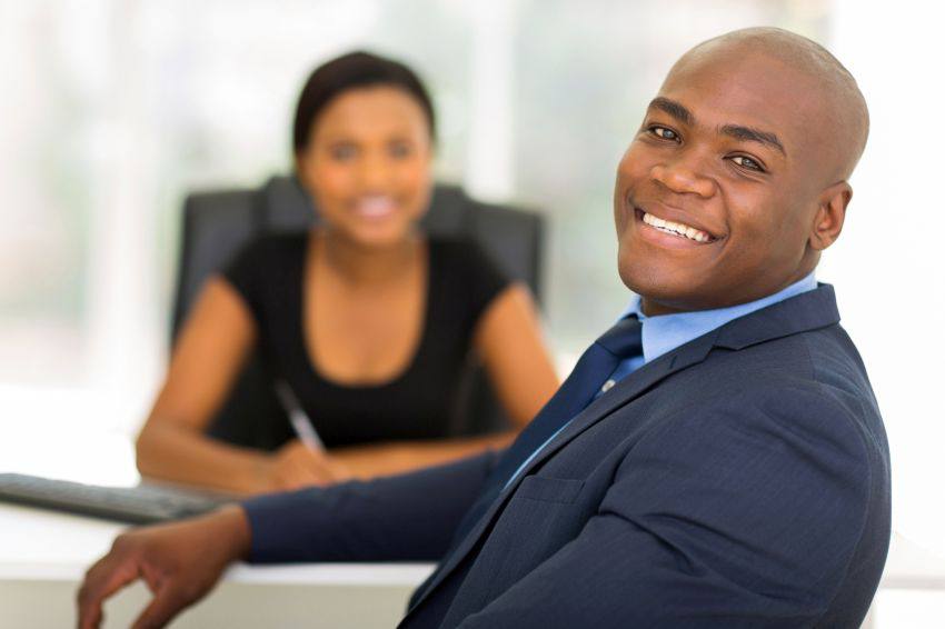 A man smiling with a woman sitting in the background