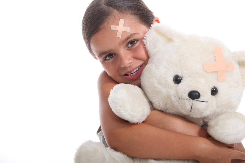 A child with a band-aid on her forehead holding a teddy bear