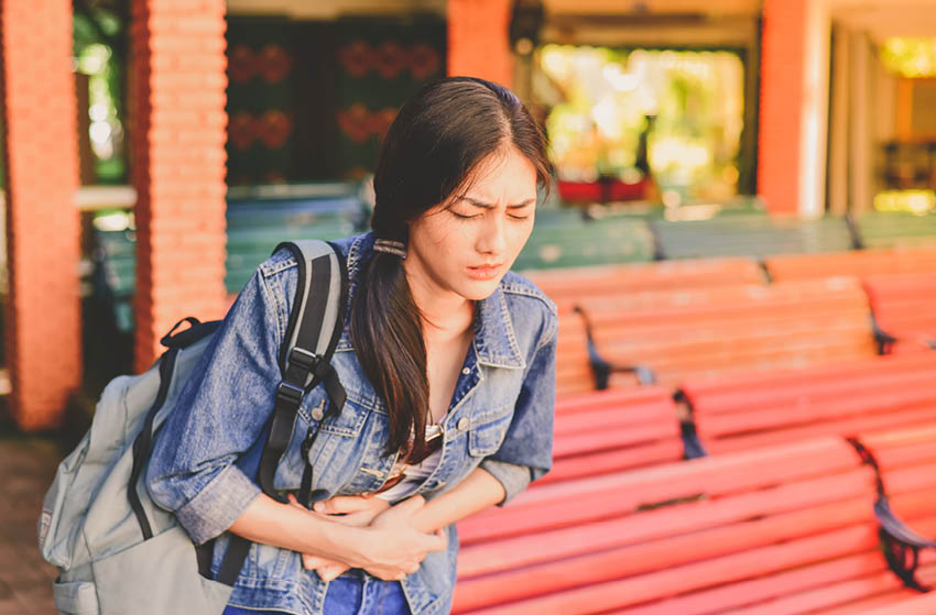 Woman holding stomach in pain while traveling