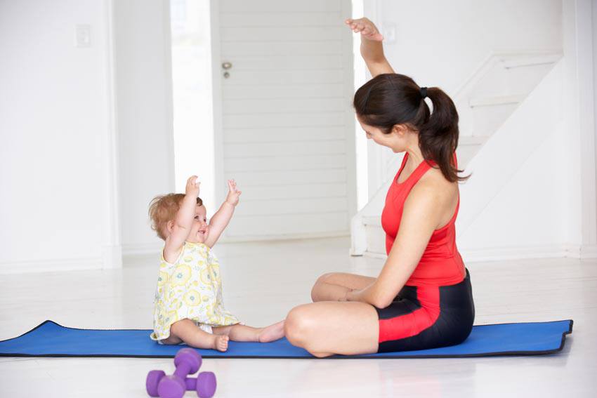 A woman and her baby sitting on a yoga mat