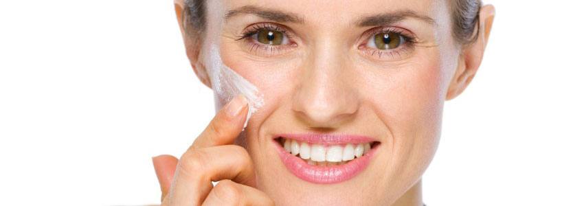 Woman applying cream on her cheek