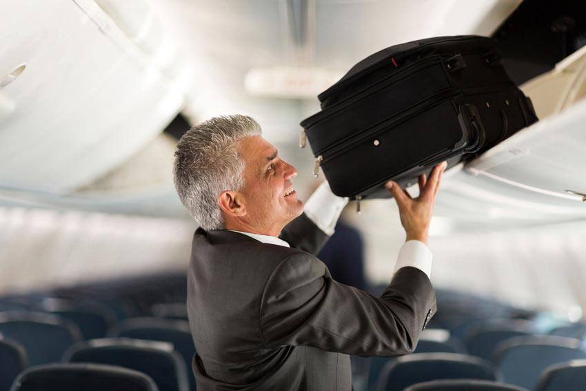 A person putting his suitcase in the compartment of airplane