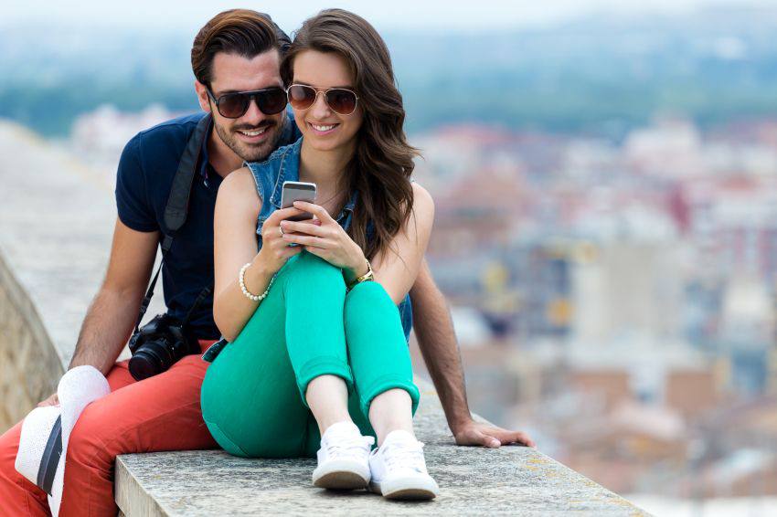 A couple sitting on an edge while looking at their phone