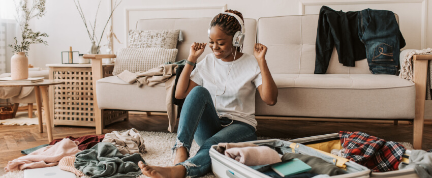 Cheerful woman with headphones packing her luggage