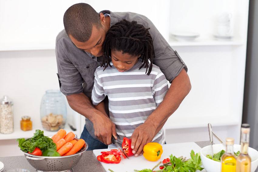 A father teaching his son how to cut vegetables