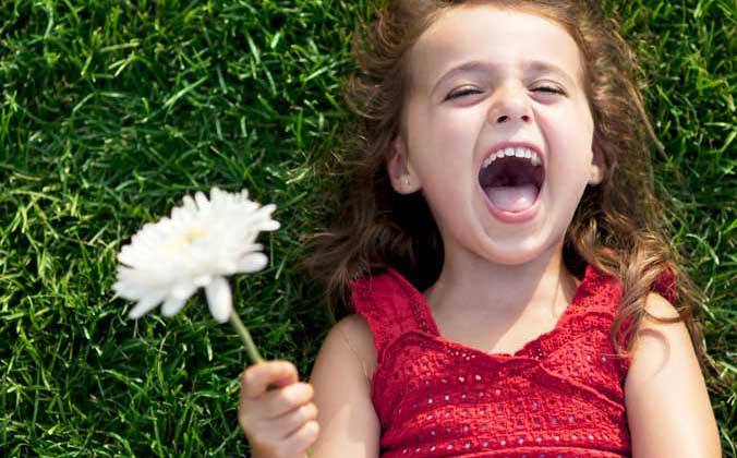 A little girl laughing holding a flower