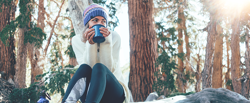 Woman holding a mug while sitting on the log