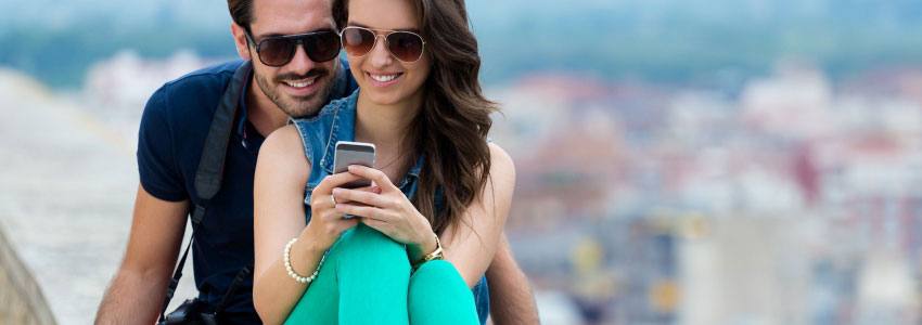 A couple sitting on an edge while looking at their phone