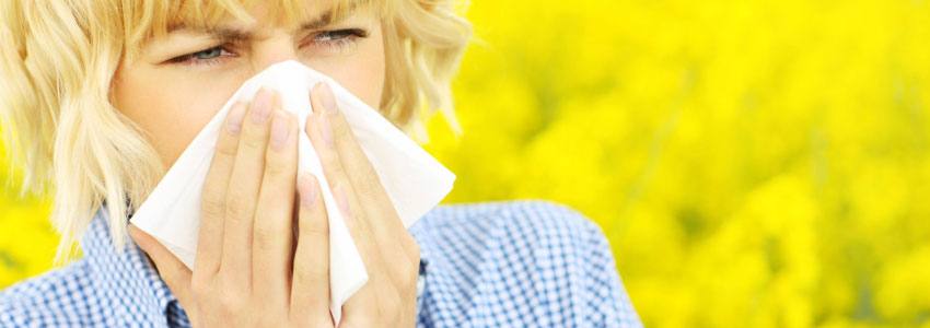 A woman in a flower field sneezing into a tissue 