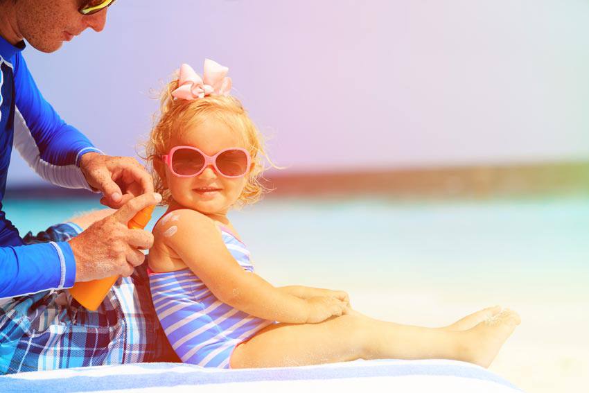 A parent applying sunscreen lotion on their child