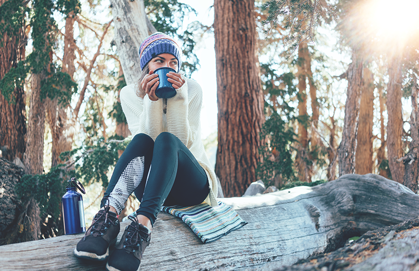 Woman holding a mug while sitting on the log