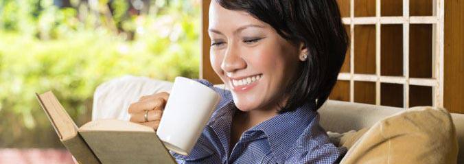 A woman holding a cup in one hand and reading a book on the other hand