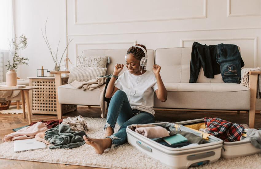 Cheerful woman with headphones packing her luggage