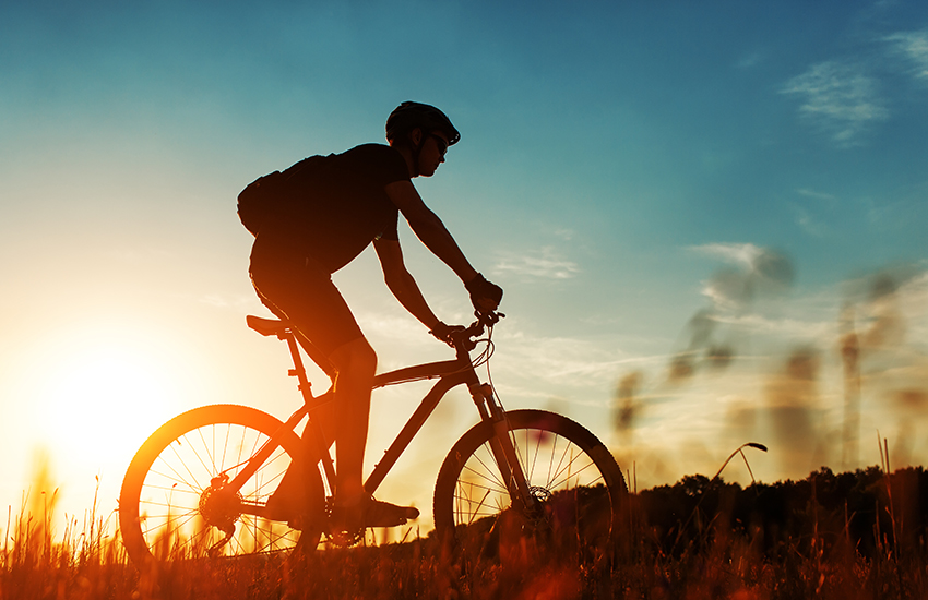  A man on a bicycle in front of the sun