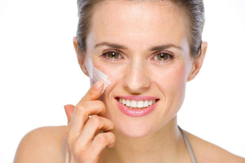 Woman applying cream on her cheek