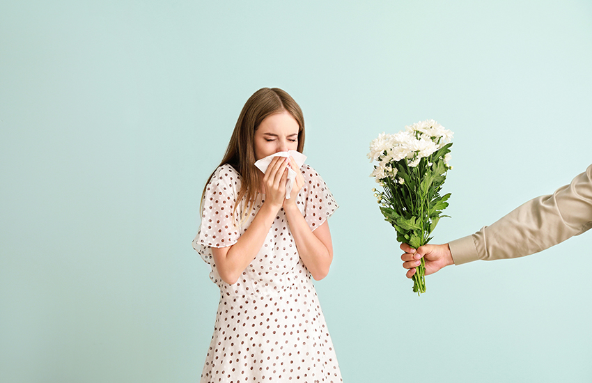 A woman sneezing into handkerchief while someone holding a bouquet of flowers