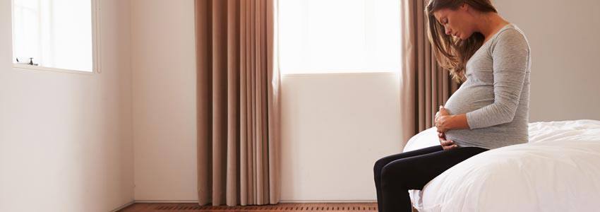 A pregnant woman sitting on a bed holding her stomach