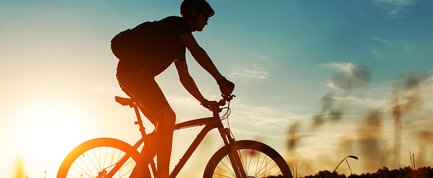  A man on a bicycle in front of the sun