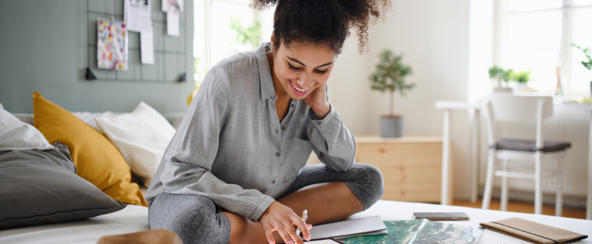 smiling woman sitting on her bed looking at her notebook