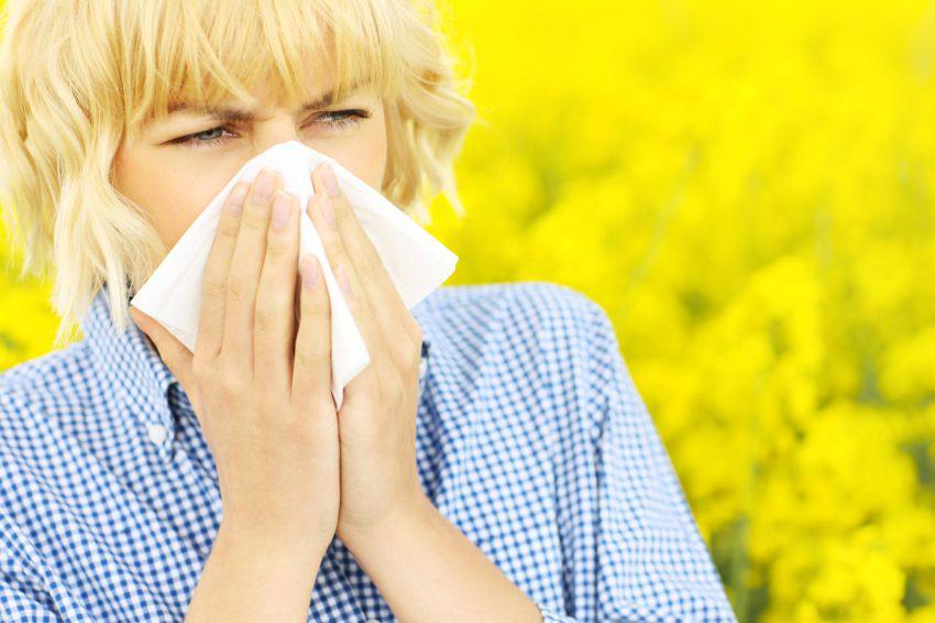 A woman in a flower field sneezing into a tissue 