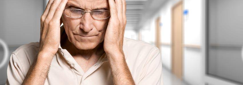 An elderly man holding his head with his hands