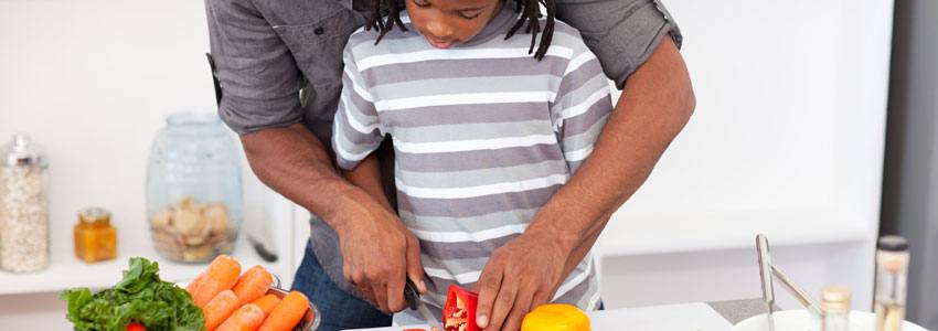 A father teaching his son how to cut vegetables