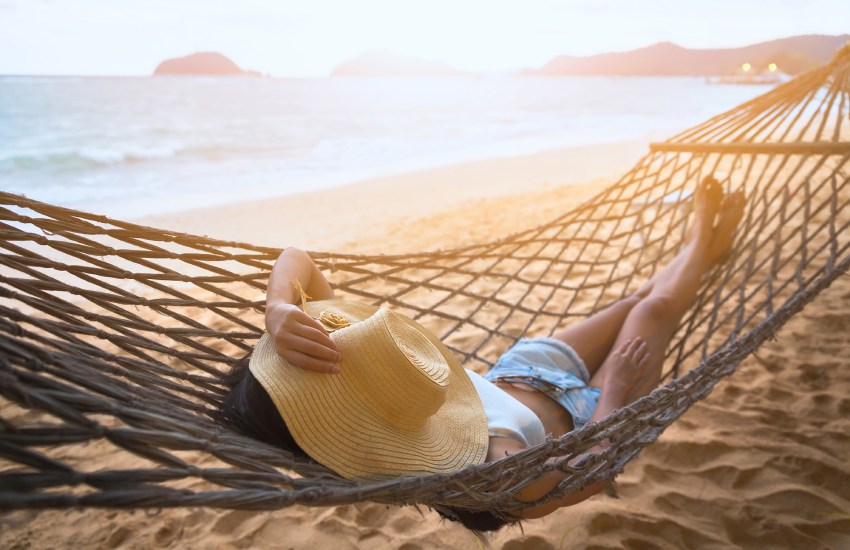 A person lying in a hammock on the beach