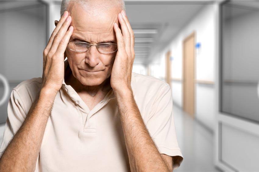 An elderly man holding his head with his hands