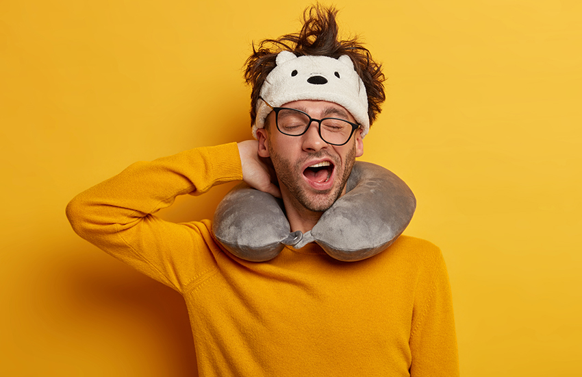 A sleepy man yawning with a neck pillow